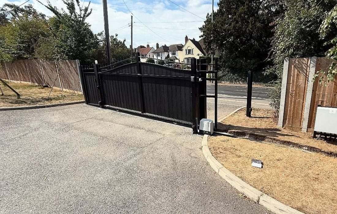 Black sliding gate across a paved entrance, the operator housing on a short post at the end of its run