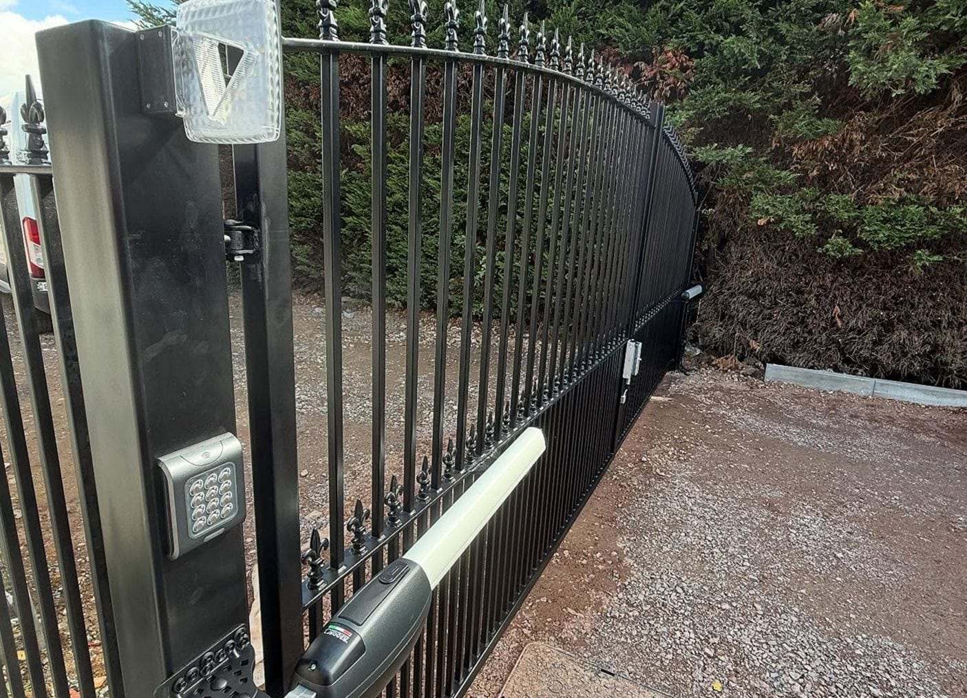 Swing gate operator arm bolted to a curved spear-top gate, a keypad and a warning light on the black gate post