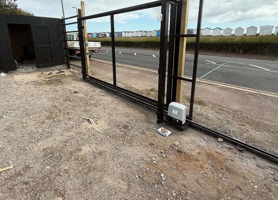 Steel frame of a new sliding gate standing on its ground track during installation, the gate motor fixed at the post