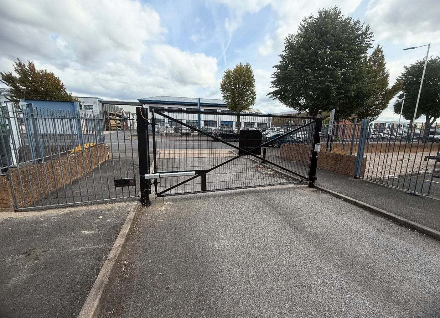 Steel swing gate across the entrance to a business parking lot, a linear opener arm on the gate post