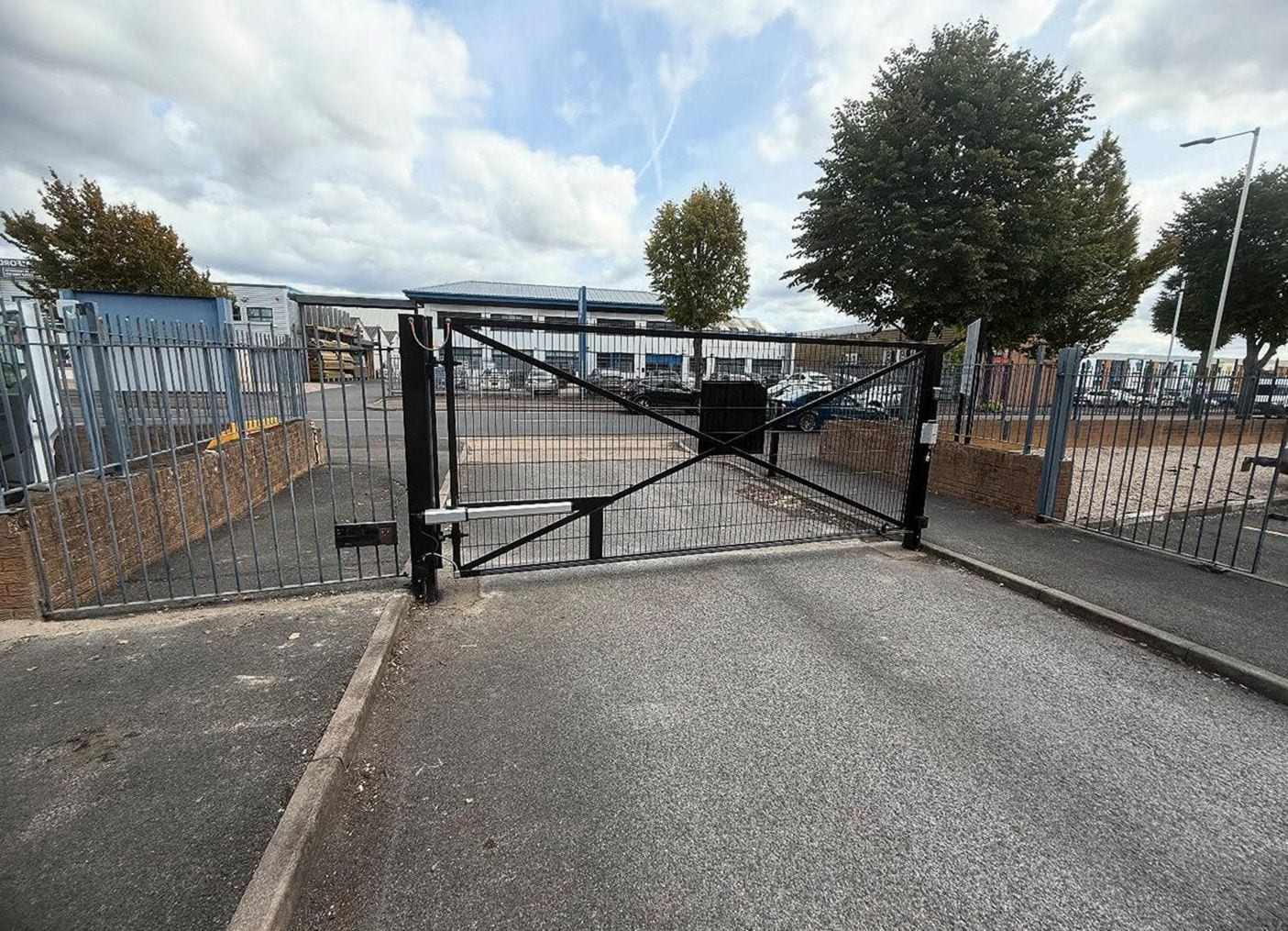 Steel swing gate across the entrance to a business parking lot, a linear opener arm on the gate post