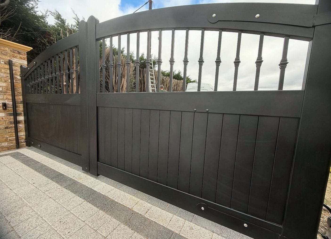 Close view of a black arched-top driveway gate, turned spindles above solid vertical boards